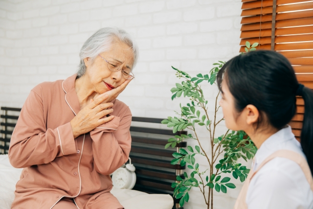 痛がる高齢者女性と介護士（虫歯） 