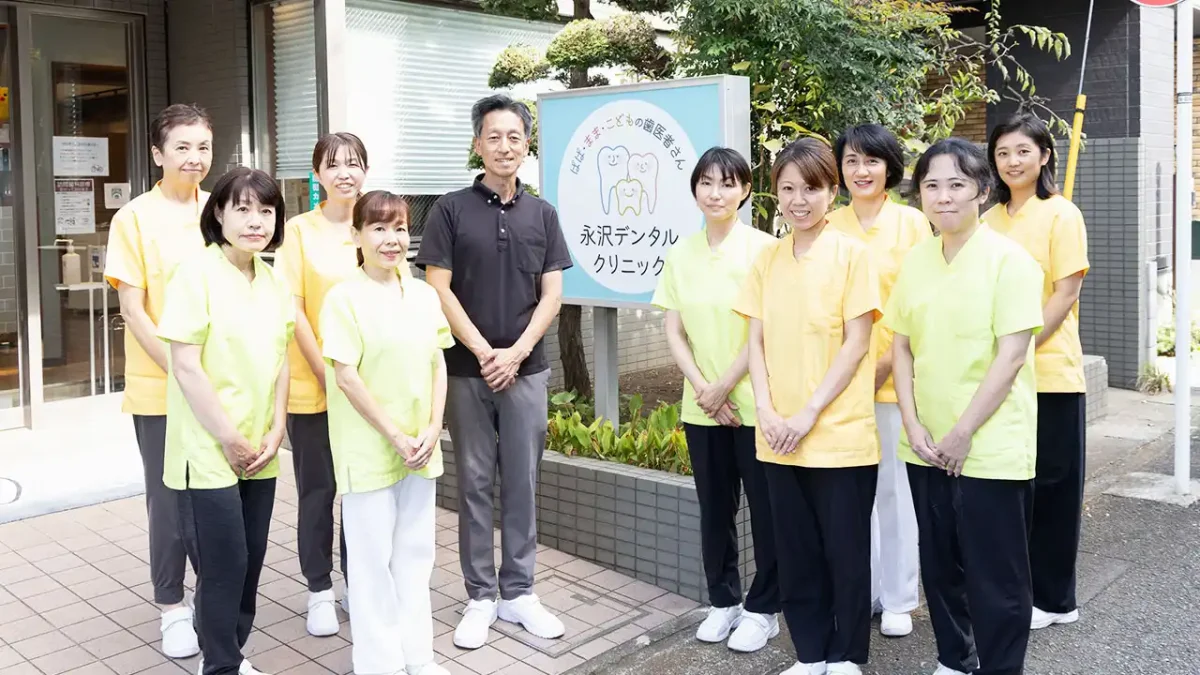 永沢デンタルクリニックの院長とスタッフが医院外の看板を挟んで並んでいる