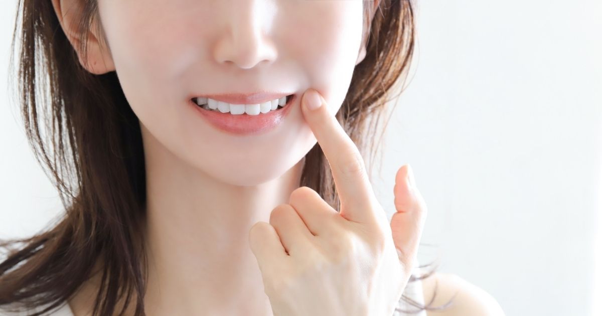 口元に指をあてて白い歯を見せる女性