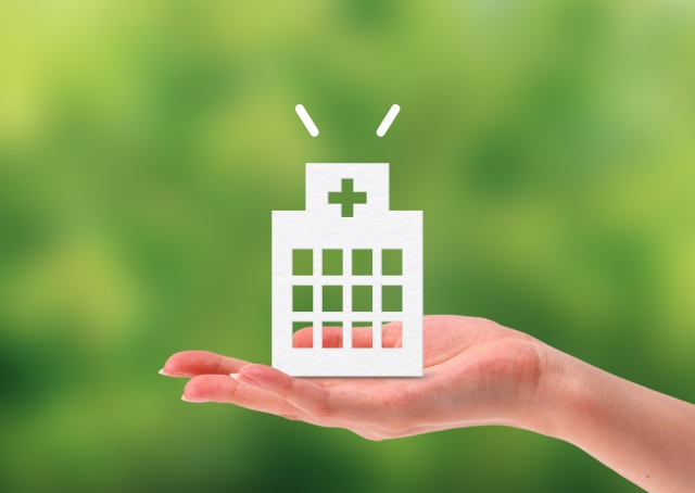 紙でできた病院を持つ女性の手