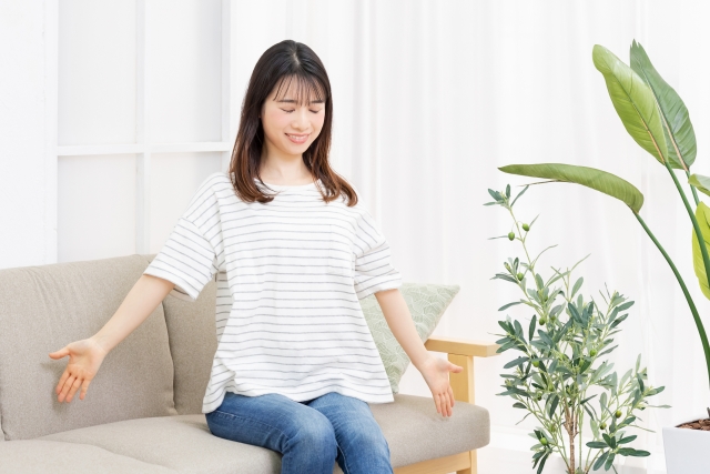 部屋のソファに座って深呼吸をする若い女性