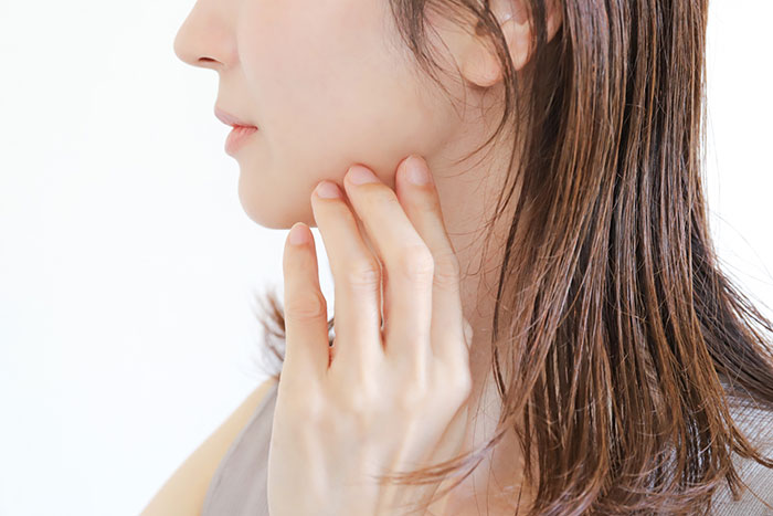 顎の不調を気にして自分の顎に手を添える女性