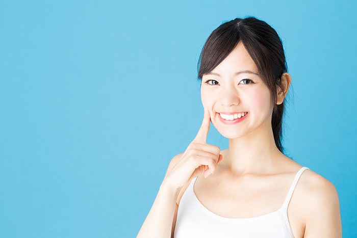 ホワイトニングした白い歯で笑顔で自分の歯指し示す女性
